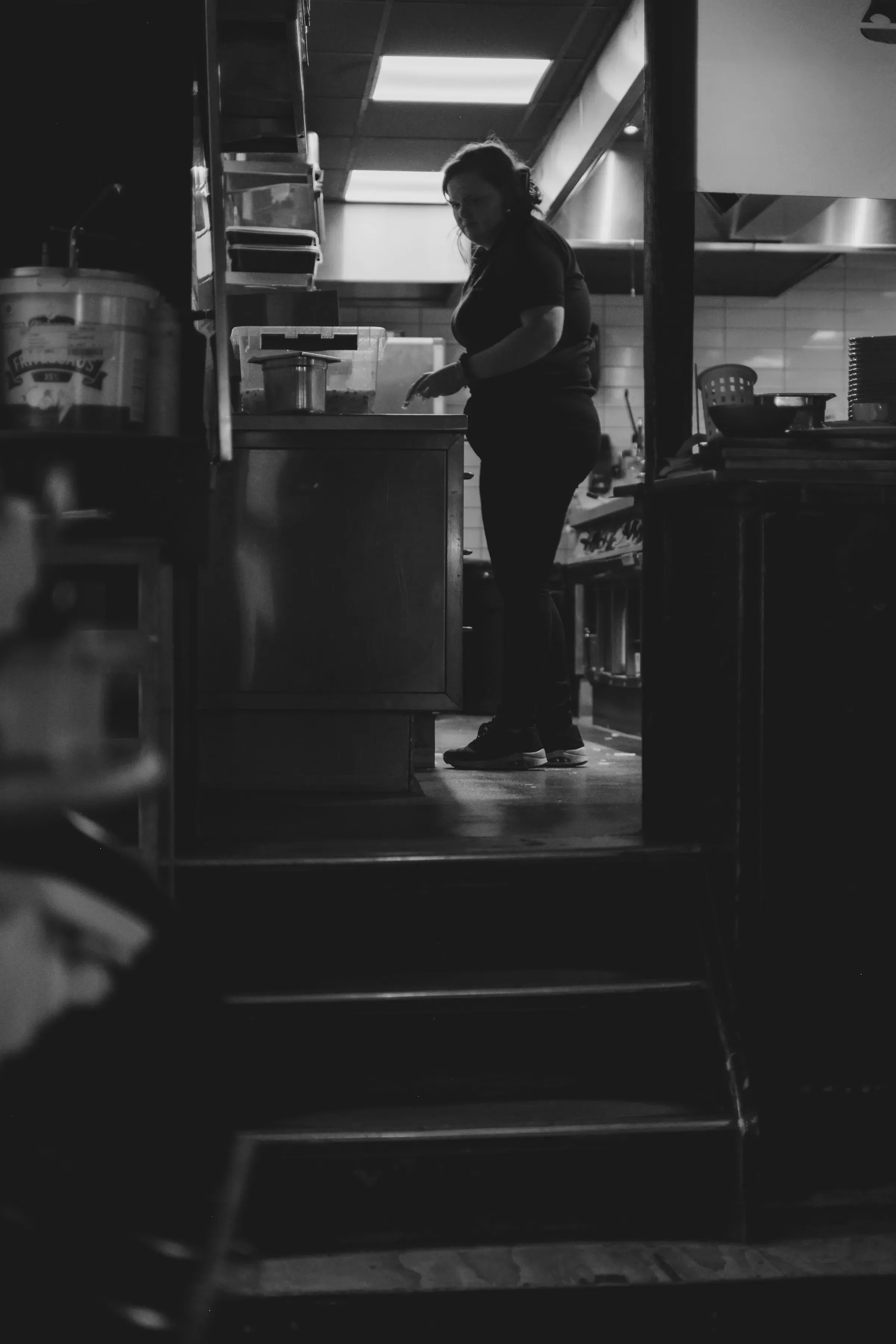 A kitchen worker at the far end of a dim service line, not looking up.
