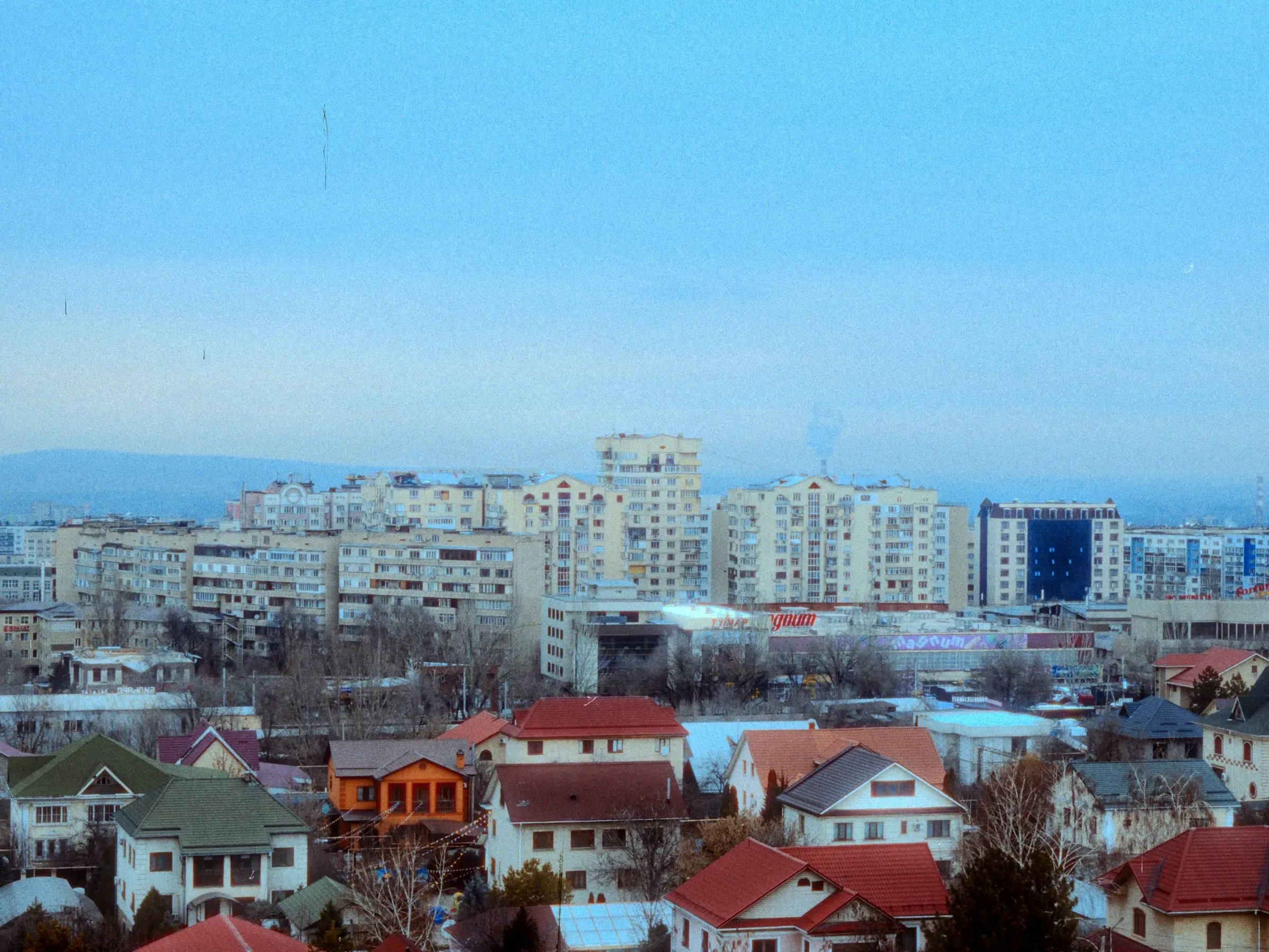 A town at dusk, apartment blocks behind a street of pitched roofs.