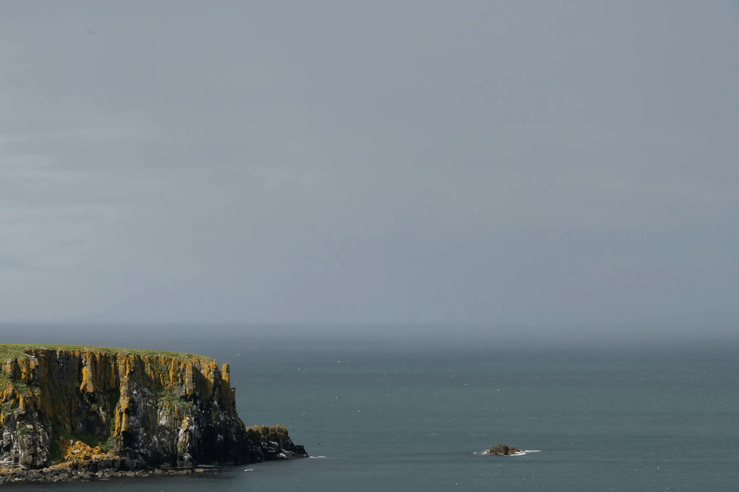A low headland at the left edge, flat grey sea, and a sky that takes two thirds of the frame.