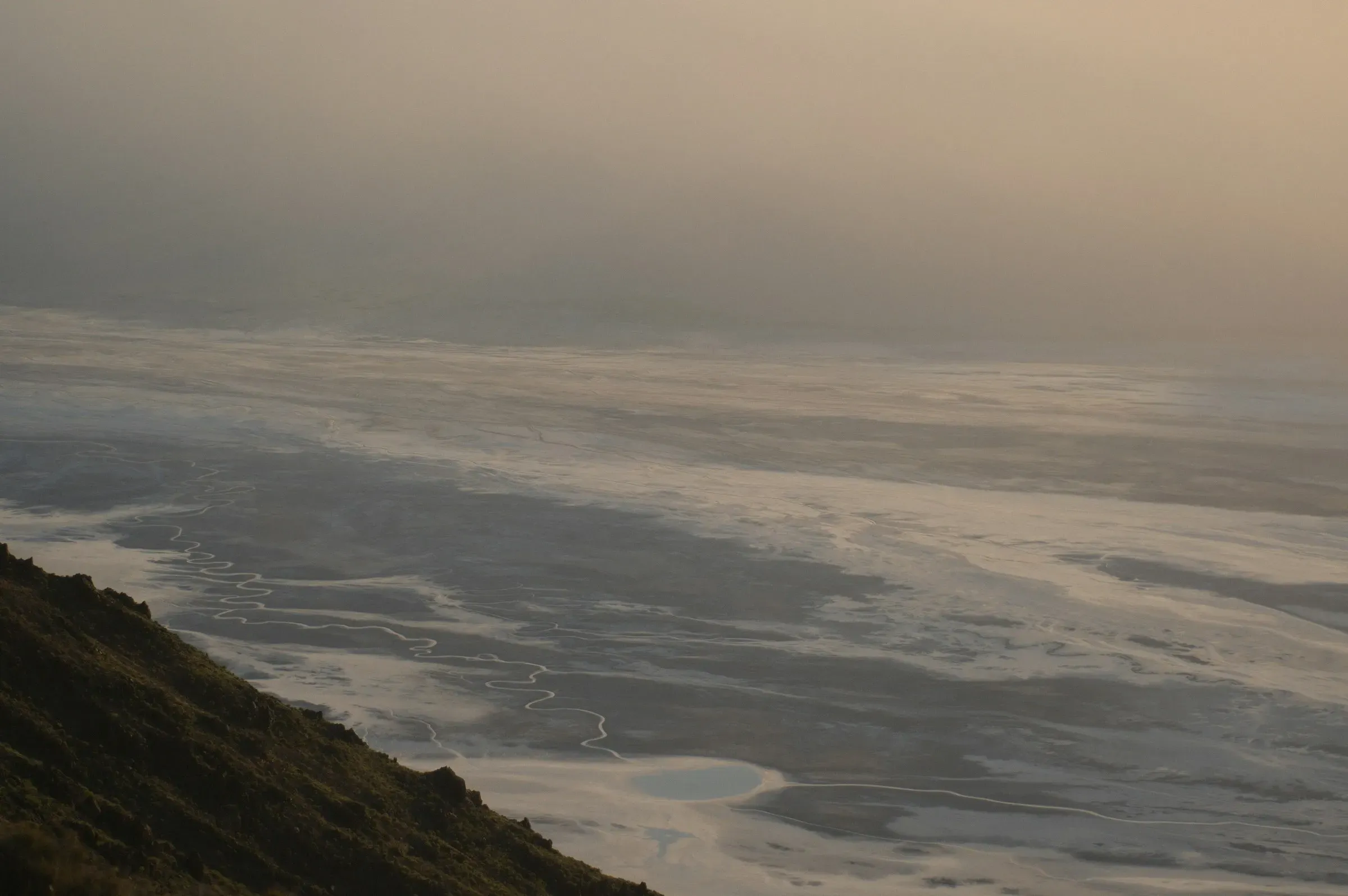 A pale flat under haze, with nothing in it but the slope it is seen from.